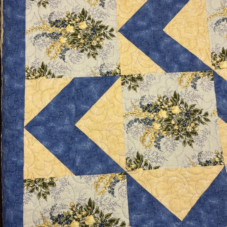 Quilt with blue and pale yellow triangular blocks and floral print panels in a geometric pattern (blue borders).